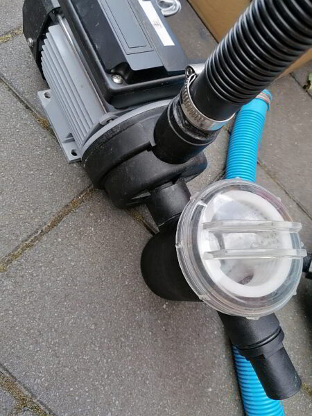 Ein kleiner Pool für den Garten. Hier: Detailansicht der Sandfilteranlage mit Pumpe, Vorfilter und angeschlossenen Schläuchen auf der Terrasse – bereit, das Poolwasser zuverlässig sauber zu halten und für sorgenfreien Badespaß im Familiengarten zu sorgen.