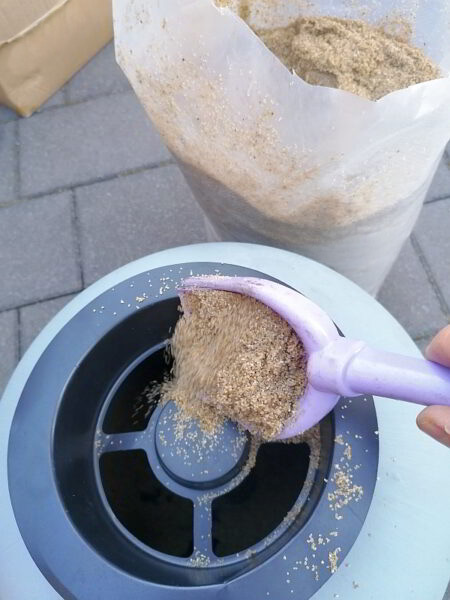 Ein Aufstellpool für den Garten. Schritt für Schritt-Anleitung. Hier: Vorbereitung für den Sommer: Feiner Filtersand wird präzise mit einer Schaufel in die Sandfilteranlage gefüllt. Ein wichtiger technischer Handgriff, damit das Poolwasser kristallklar bleibt und der gemeinsame Badespaß für die ganze Familie endlich losgehen kann.