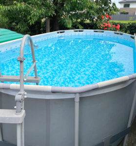 Hier zu sehen ein großer ovaler Aufstellpool mit Wasser gefüllt und Blumen und Bäumen im Hintergurnd. Es geht hier um den Vergleich von Kartuschen- und Sandfiltern für einen Aufstellpool.