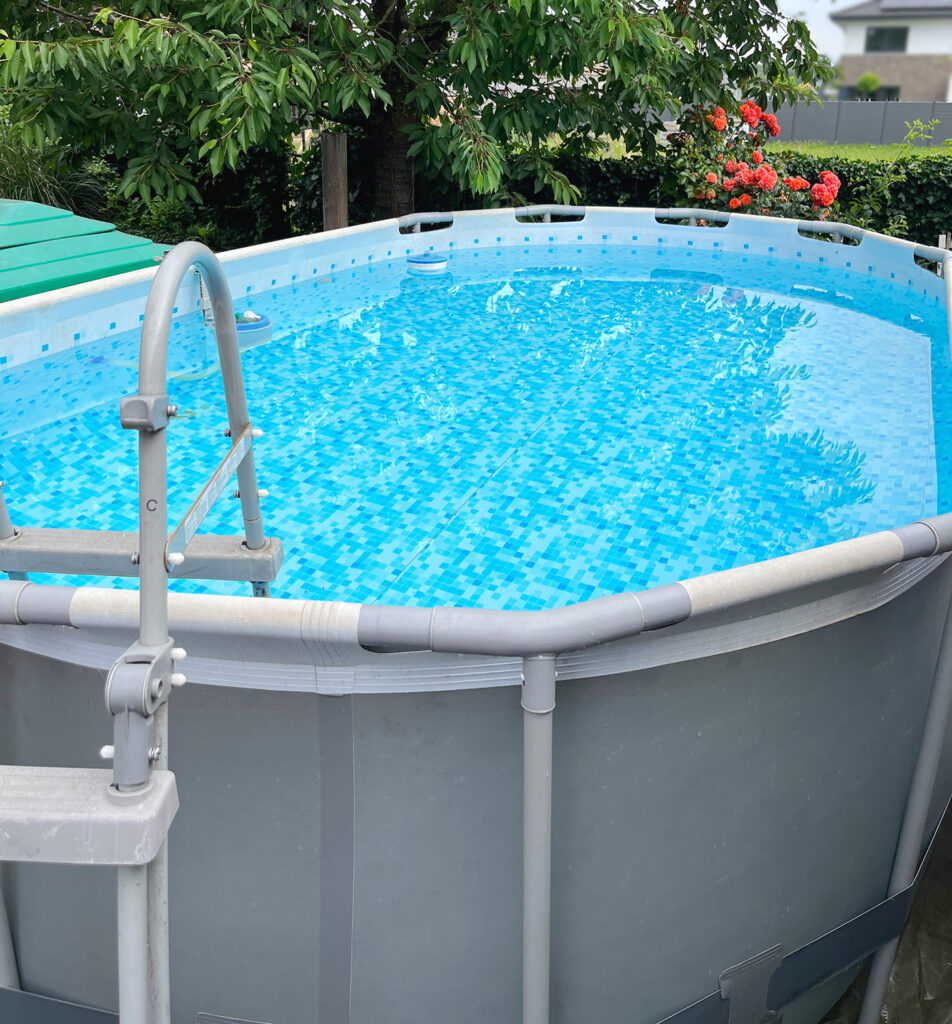 Hier zu sehen ein großer ovaler Aufstellpool mit Wasser gefüllt und Blumen und Bäumen im Hintergurnd. Es geht hier um den Vergleich von Kartuschen- und Sandfiltern für einen Aufstellpool.
