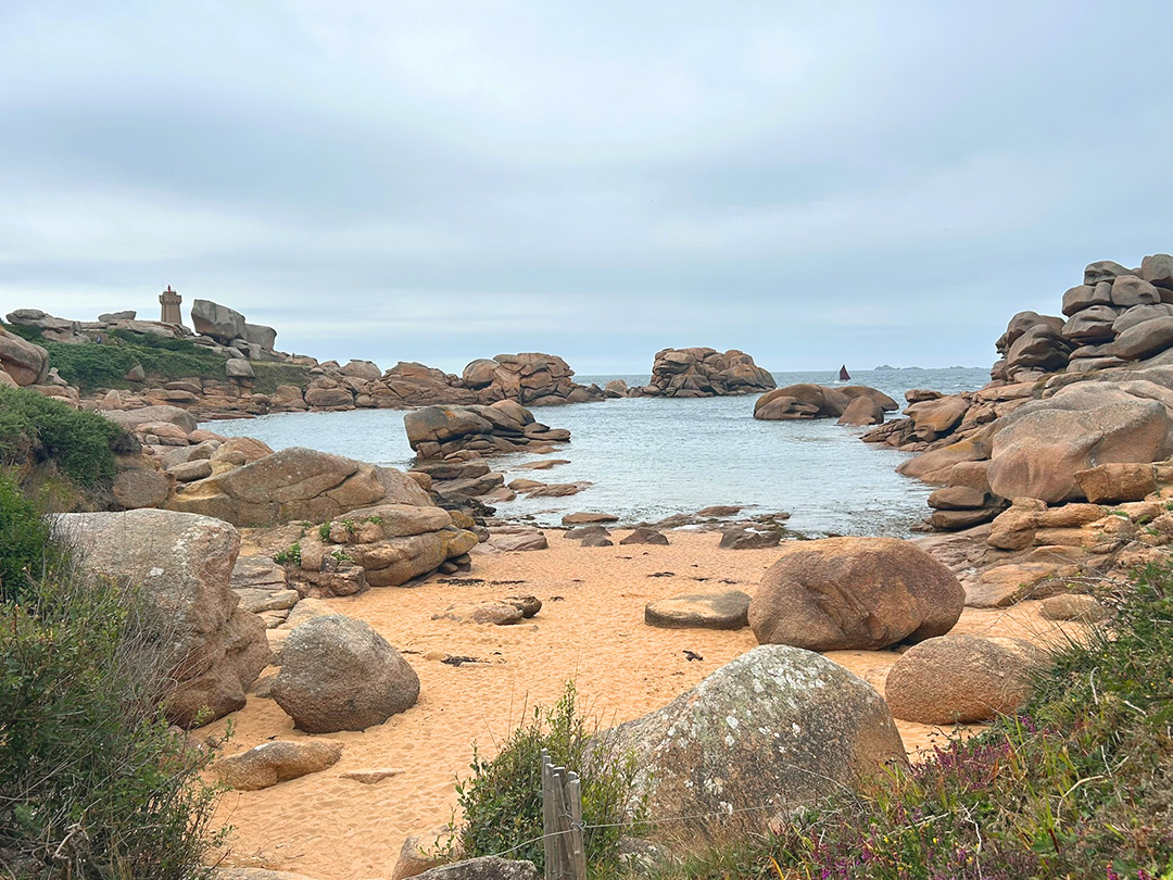 Bretagne mit Kindern - Westküste Cote de Granit Rose - Großes Felsbecken, mit rötlichen Sand davor. Im Hintergrund erkennbar: Der Leuchtturm "Phare de Ploumanac’h". Er steht bei Ploumanac’h/Perros-Guirec direkt zwischen den rosafarbenen Granitfelsen und markiert die Einfahrt zum Hafen.