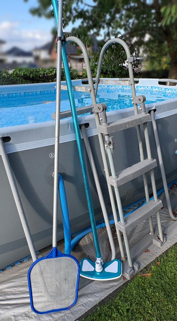 familie-entdeckt.de - Pool-Pflege, hier zu sehen: Poolleiter mit Poolkescher, Bodensauger und Saugschlauch an einem oberirdischen Gartenpool.