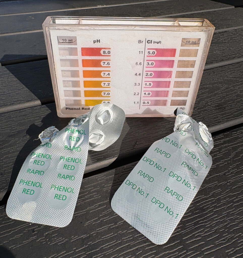 familie-entdeckt.de - Wie Poolwasser testen - Anleitung für einen Pool-Tester - Zwei geöffnete Testtablettenstreifen und eine Farbskala für die Wasseranalyse liegen auf einem dunklen Tisch, zur Prüfung von Pool- oder Wasserwerten.